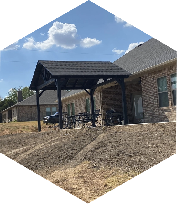 Black pergola with a brick house in the background.